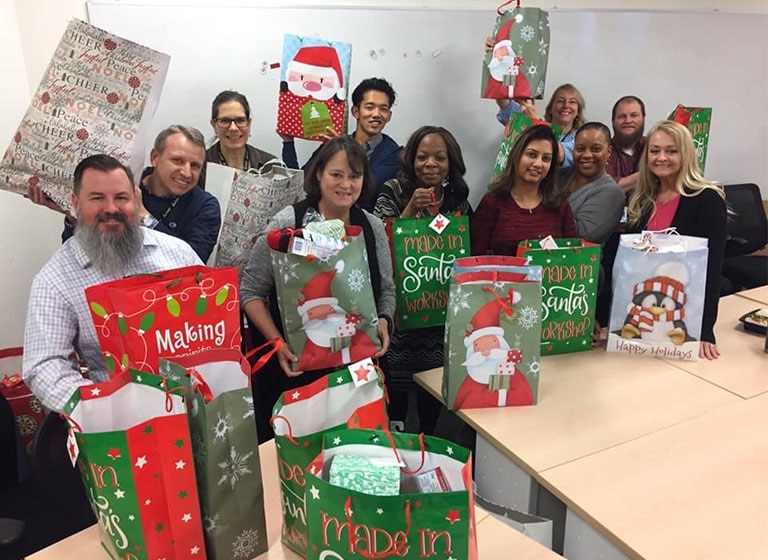 Eleven smiling Mitsubishi Electric volunteers hold holiday gift bags filled with presents.